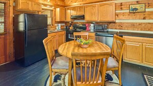 A wooden cabin kitchen with a black refrigerator, wooden cabinets, a microwave, and a dining table with chairs. - Peace, Quiet, and a Cozy Cabin (Sevierville)
