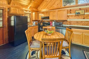 A wooden cabin kitchen with a black refrigerator, wooden cabinets, a microwave, and a dining table with chairs. - Peace, Quiet, and a Cozy Cabin (Sevierville)