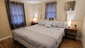 Un dormitorio con una cama grande, dos mesitas de noche con lámparas, un cabecero y una obra de arte colgada en la pared.