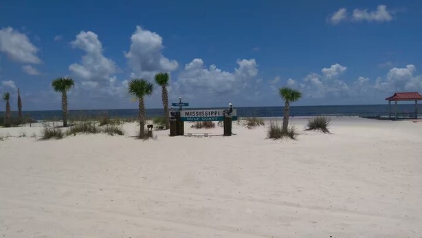 Una playa con un cartel que dice "Mississippi Gulf Coast" y una estructura de techo rojo al fondo.