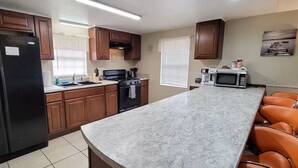 Una cocina con armarios de madera, un refrigerador negro, una estufa, un microondas y una encimera de mármol.