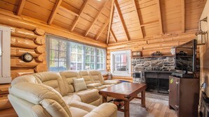 A log cabin interior with a sofa, a fireplace, and a television. - Cozy Paradise - Four Bedroom Cottage, Sleeps 8 (Ryerson)
