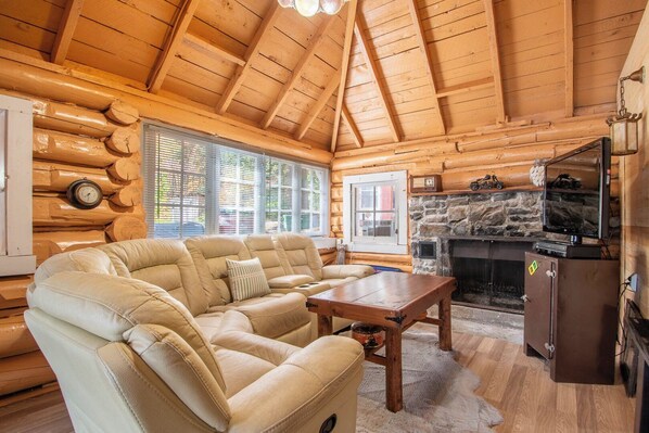 A log cabin interior with a sofa, a fireplace, and a television.