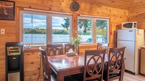A wooden cabin with a dining table, chairs, a clock, a microwave, and a view of a lake. - Cozy Paradise - Four Bedroom Cottage, Sleeps 8 (Ryerson)