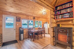A cozy cabin interior with a wooden interior, a dining area with a table and chairs, a kitchen with a microwave and refrigerator, and a bookshelf filled with books.
