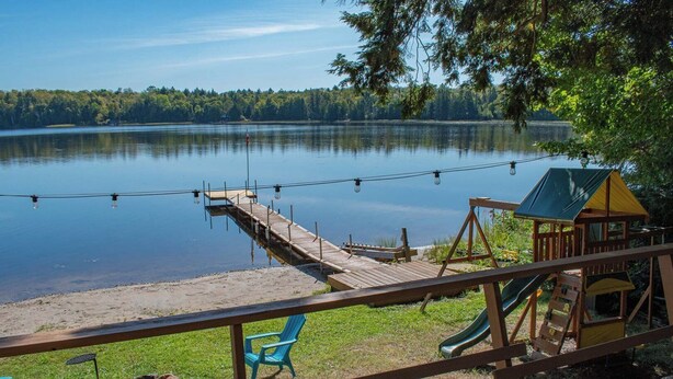 A lakeside deck with a wooden walkway, a play structure, and seating areas. - Cozy Paradise - Four Bedroom Cottage, Sleeps 8 (Ryerson)