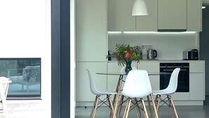Une cuisine moderne avec des meubles blancs, une table à manger avec des chaises, un luminaire suspendu et un vase rempli de fleurs.