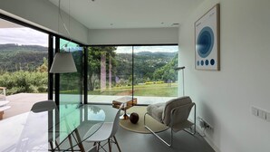 Een moderne kamer met een glazen tafel, stoelen, een bank en uitzicht op een groen landschap.