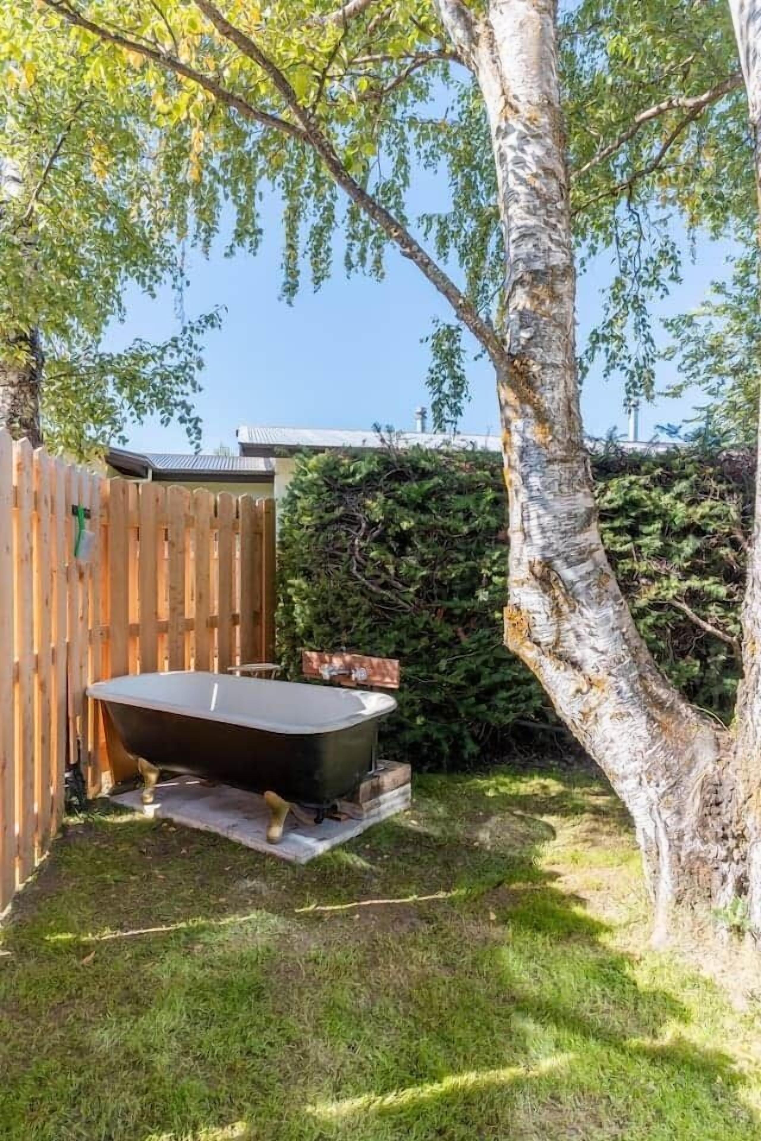 A hot tub in a backyard with a wooden fence and a tree.