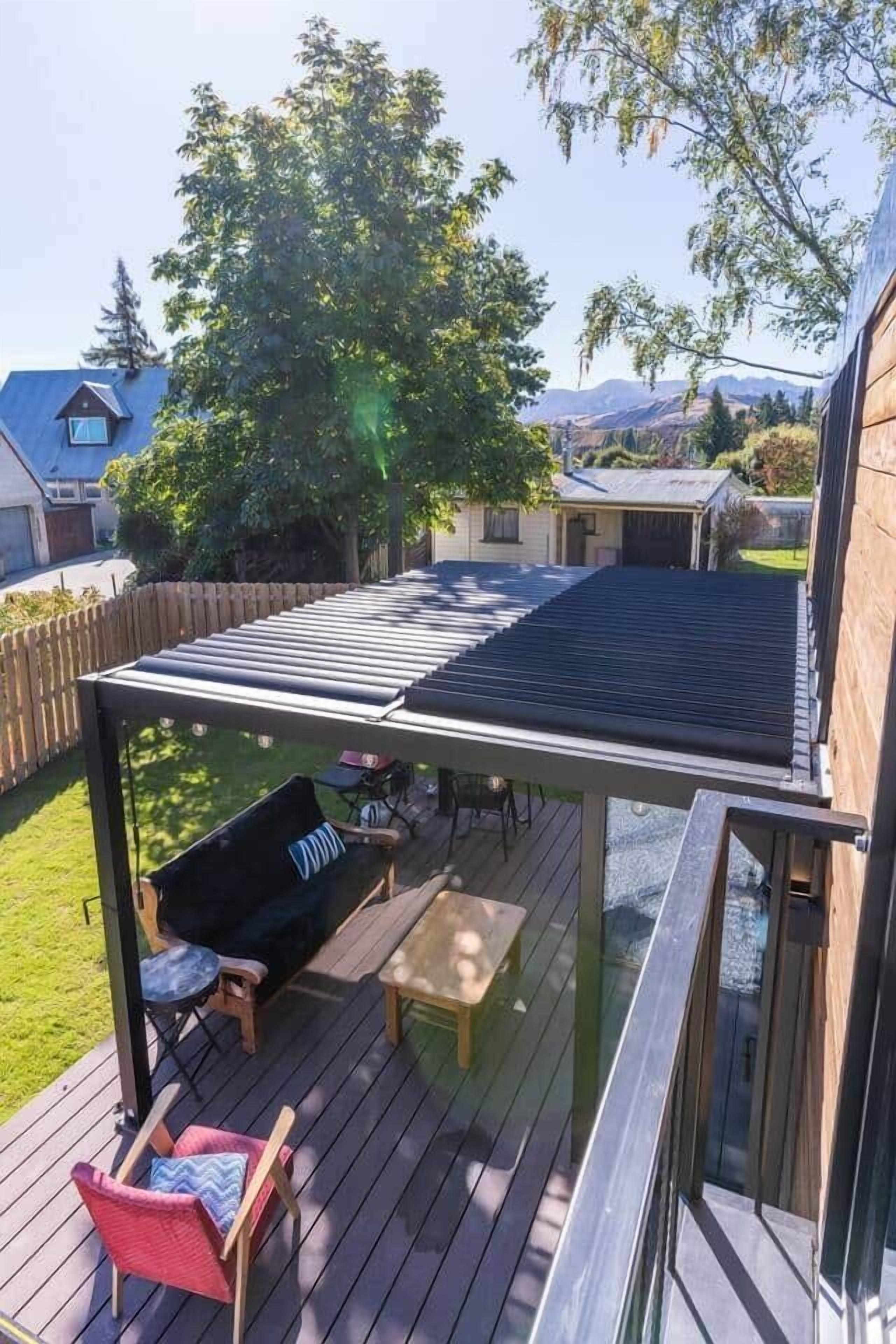 Eine überdachte Terrasse mit Tisch, Stühlen und einer Hängematte, mit Blick auf einen Baum und Berge im Hintergrund.