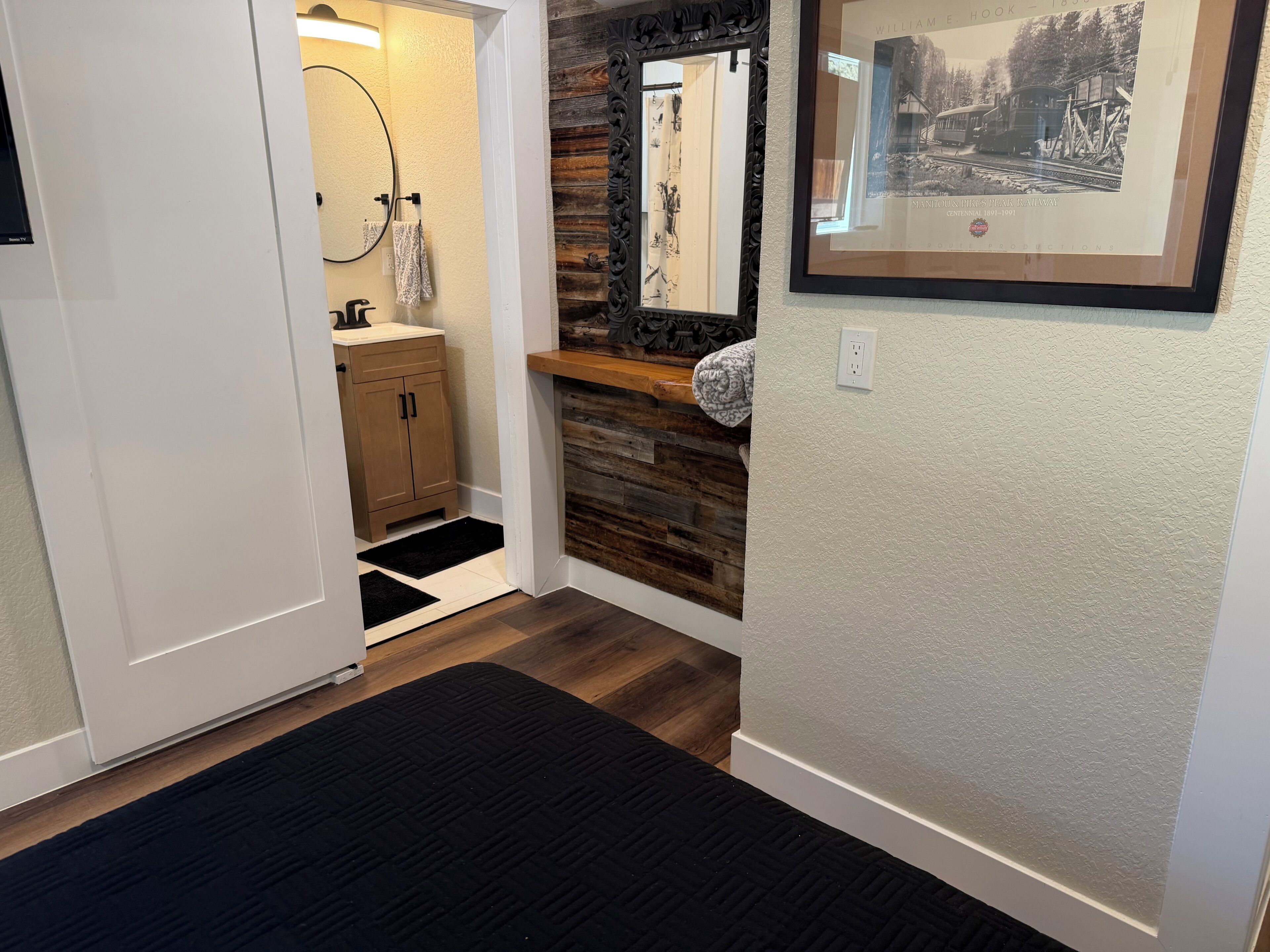 A hallway with a wooden floor, a black rug, a wooden cabinet, a mirror, and a framed picture on the wall.