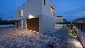 Ein modernes, zweistöckiges Haus mit großer Garage, Schwimmbad und gut beleuchteter Auffahrt.