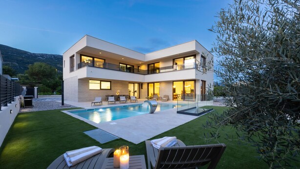 Ein modernes, zweistöckiges Haus mit Swimmingpool, Sitzgelegenheiten im Freien und einem gepflegten Rasen.