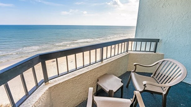Un balcon avec vue sur l’océan, une petite table et deux chaises.