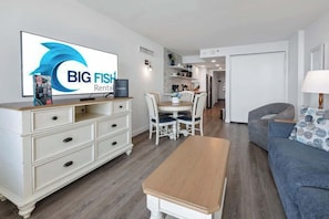 Ein modernes Wohnzimmer mit Fernseher, weißen Möbeln, einem Essbereich und einer Couch.
