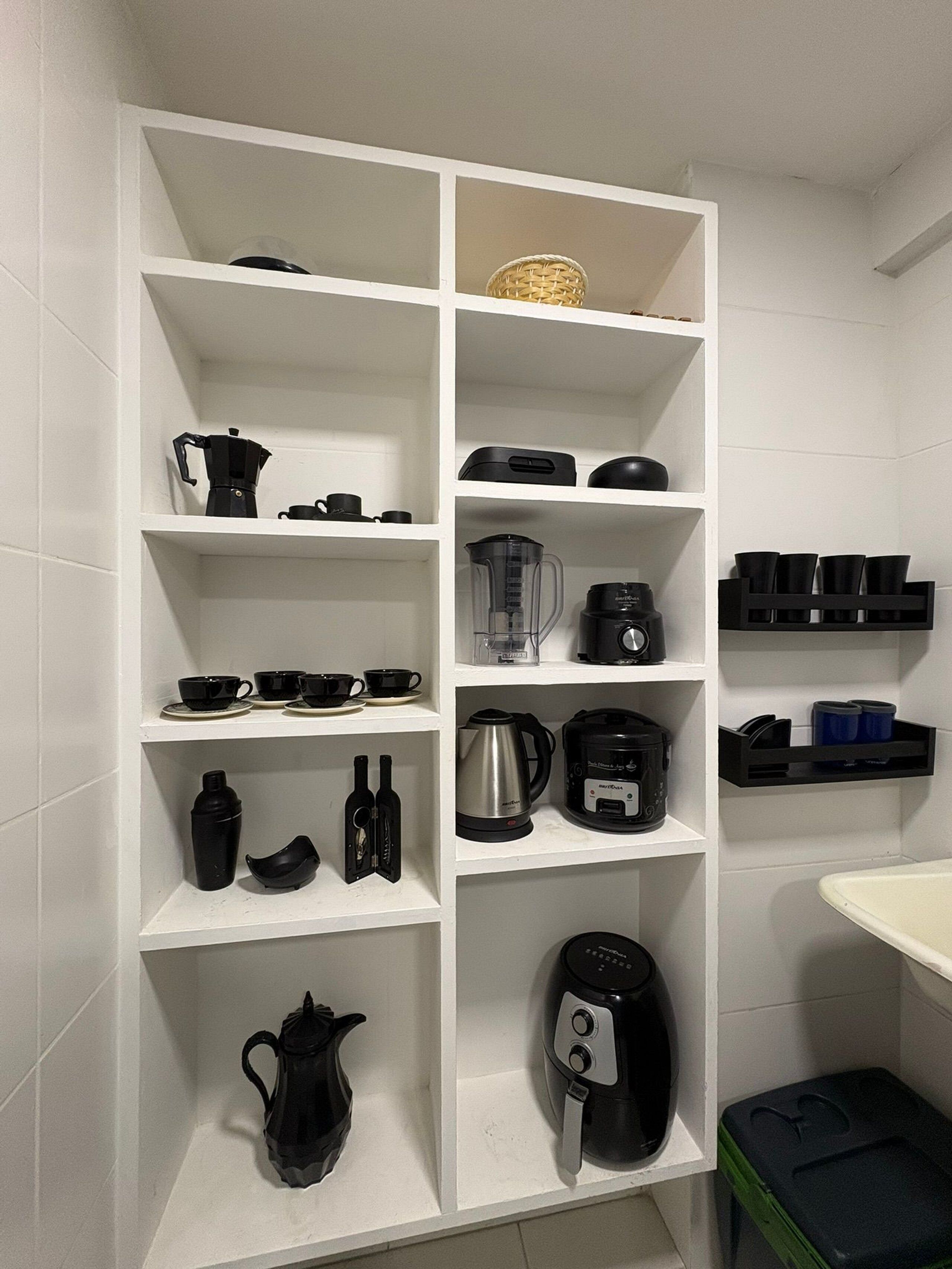 A kitchen with white shelves containing various black kitchen appliances and utensils.