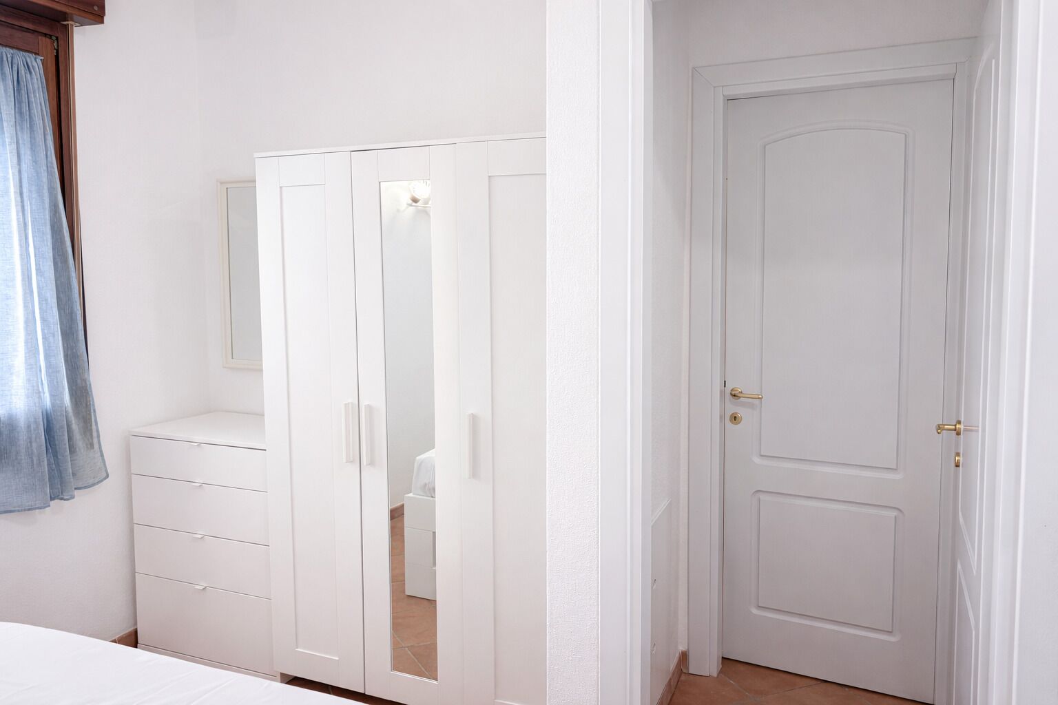 A bedroom with a white wardrobe, a bedside table, and a door.