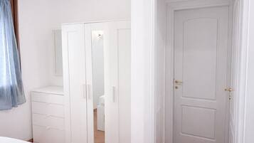 A bedroom with a white wardrobe, a bedside table, and a door.