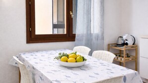 Ein Essbereich mit Tisch für zwei Personen, einer Obstschale und einer Küchenzeile mit Wasserkocher und Kaffeemaschine.