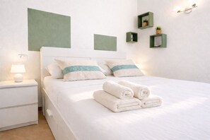 Una cama bien hecha con sábanas blancas y dos almohadas, una lámpara de noche y una mesita de noche.