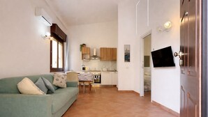 Ein Wohnzimmer mit einem grünen Sofa, einem Esstisch und einer Küche im Hintergrund.