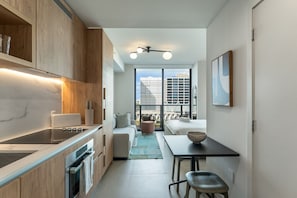 A compact kitchen with wooden cabinets, a built-in oven, and a dining area with a table and chairs. - Crosby Miami WTC Studio Sunset #1215 (Miami)