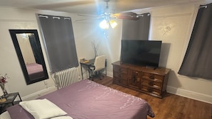 Une chambre à coucher comprenant un lit, un bureau, une chaise, un téléviseur et un ventilateur de plafond.