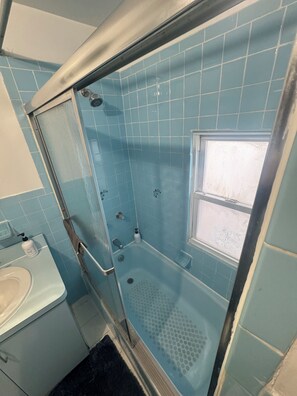 A bathroom with a glass-enclosed shower, a sink, and a window.