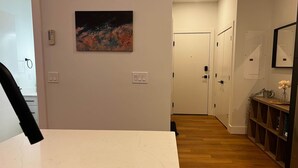 Käytävä, jossa on valkoinen seinä, taulu, valkoinen ovi, puulattia ja hylly, jossa on maljakko.