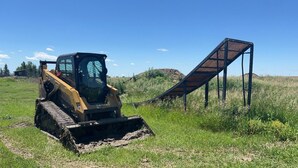 A construction vehicle on a dirt path with a metal structure in the background. - The Slayground of the Dakotas Private MX Retreat (Dickinson)