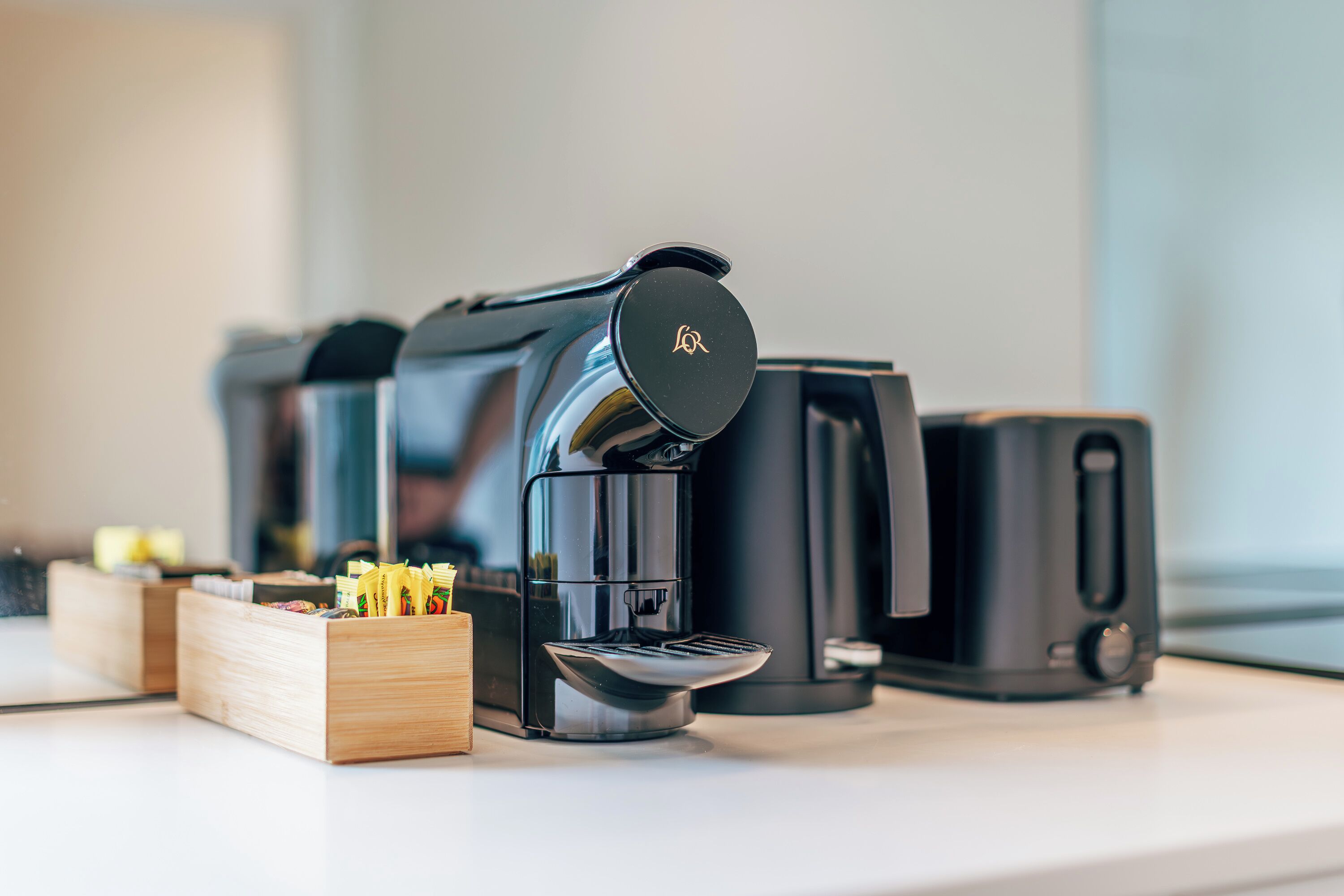 A coffee machine with a black lid and a logo, a coffee maker, and a coffee pot on a countertop.