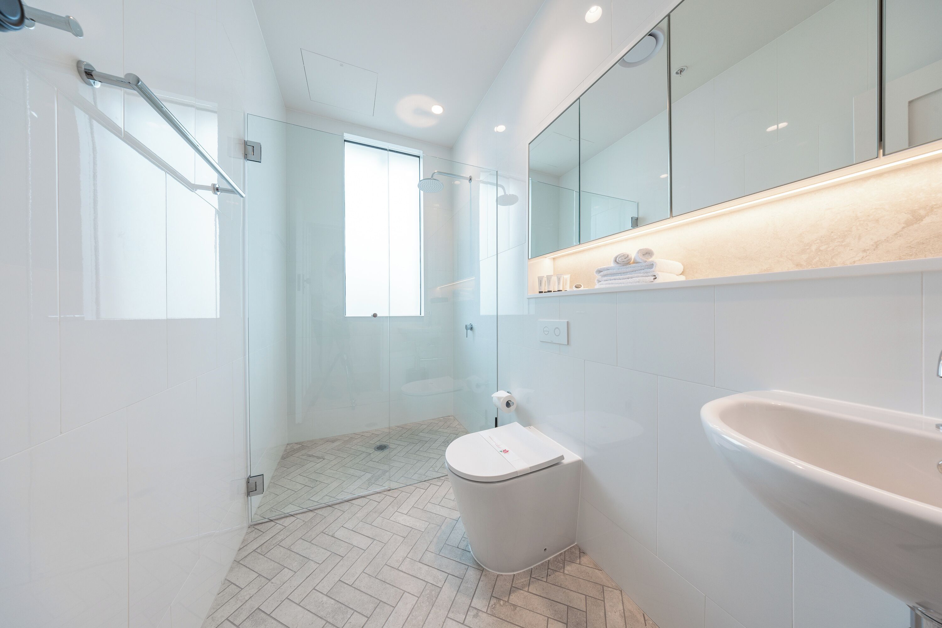 A modern bathroom with a glass shower enclosure, a white toilet, a sink, and a mirror.