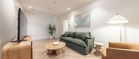 A modern living room with a green sofa, a round wooden coffee table, a beige armchair, and a floor lamp.