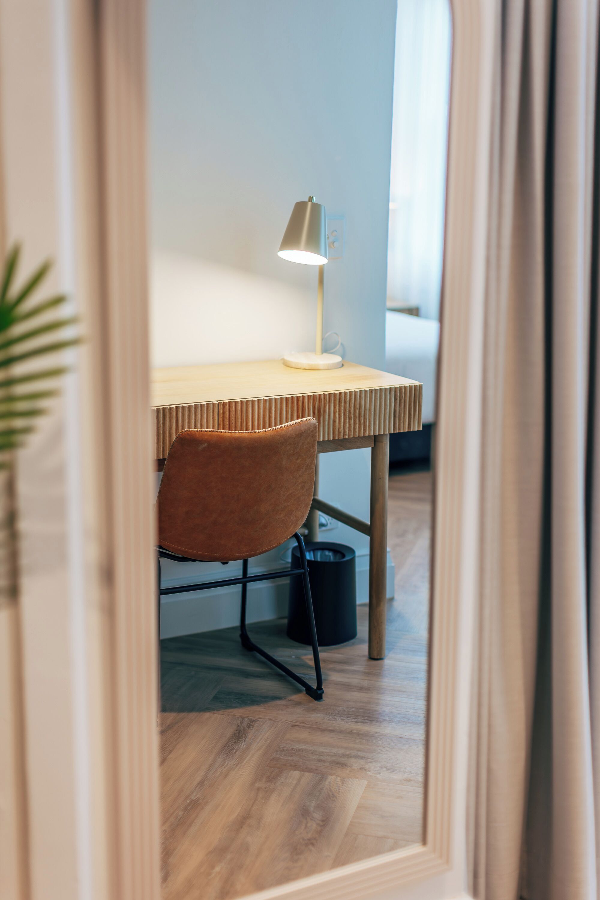 Een moderne kamer met een houten bureau, een bruine stoel, een vloerlamp en een zwarte prullenbak.