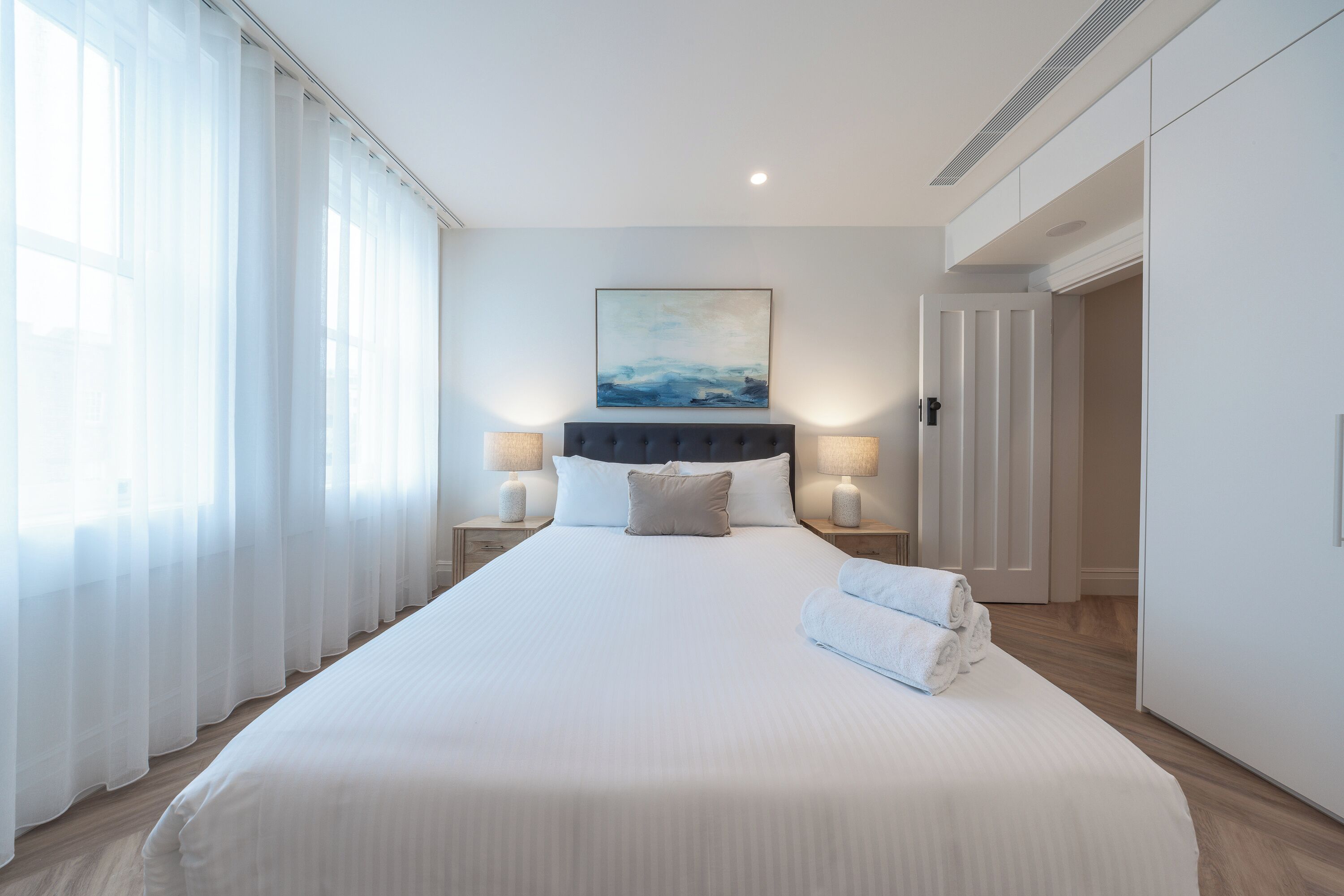 Ein modernes Hotelzimmer mit einem großen Bett, einem Bild an der Wand und Meerblick durch das Fenster.
