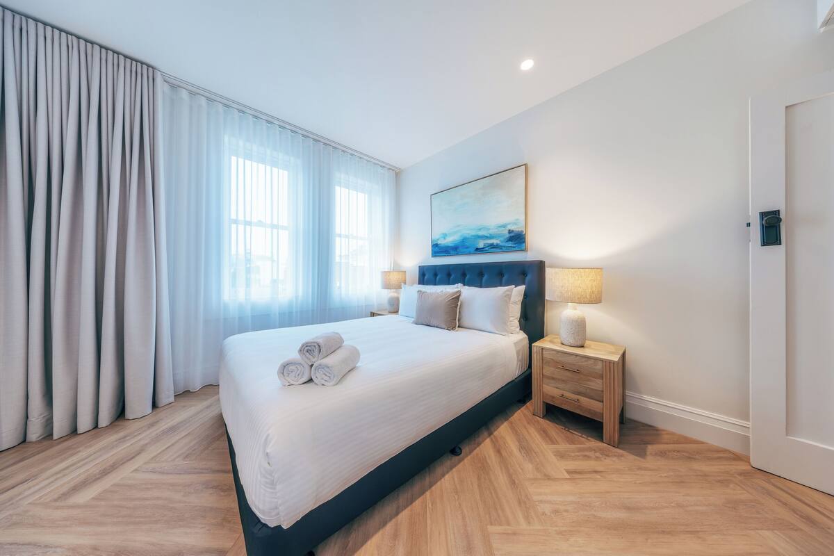 Ein Hotelzimmer mit einem großen Bett, einem Kopfteil, einem Nachttisch, einer Lampe und einem Bild an der Wand.