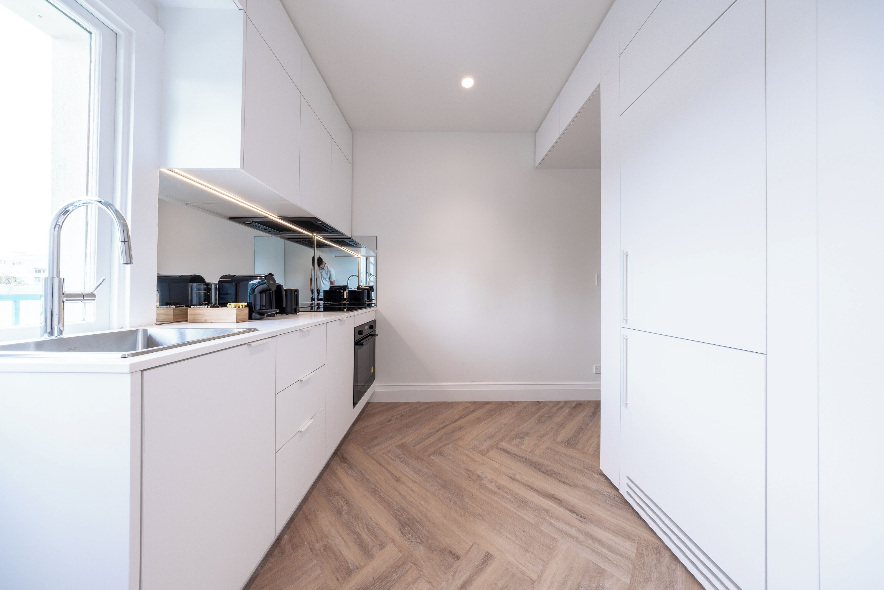A modern kitchen with white cabinetry, a stainless steel sink, and a herringbone wood floor.