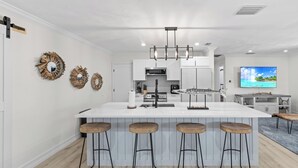 A modern kitchen with a central island, bar stools, and a flat-screen TV mounted on the wall. - Greek-style beach oasis. Close drive to the beach and Mercato (Naples)