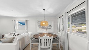 A dining area with a round wooden table, white chairs, and a hanging light fixture. - Greek-style beach oasis. Close drive to the beach and Mercato (Naples)