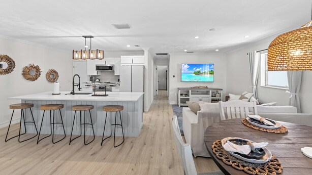 A modern kitchen with white cabinets, a central island with stools, and a dining area with a round table and woven placemats. - Greek-style beach oasis. Close drive to the beach and Mercato (Naples)