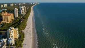 An aerial view of a coastal area with a long sandy beach, adjacent high-rise buildings, and a clear view of the ocean. - Greek-style beach oasis. Close drive to the beach and Mercato (Naples)
