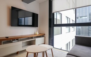 A modern room with a large TV, a wooden console table, a white sofa, and a large window offering a city view. - w* | Deluxe 1BR Apartment in Heart of San Isidro (San Isidro)