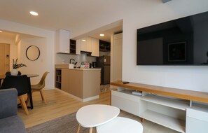 A modern living room with a flat-screen TV, a dining area with chairs, a kitchen with cabinets, and a small island with a coffee machine. - w* | Deluxe 1BR Apartment in Heart of San Isidro (San Isidro)