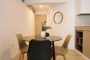A modern dining area with a glass table, two chairs, a vase with a plant, and a wooden door in the background. - w* | Deluxe 1BR Apartment in Heart of San Isidro (San Isidro)