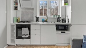 Uma cozinha compacta com armários brancos, fogão a gás, micro-ondas e máquina de lavar louça.