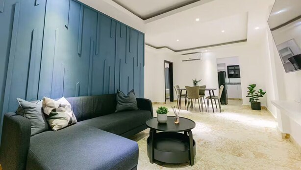 A modern living room with a dark grey sofa, a round coffee table, and a blue accent wall. - Penthouse con dos camas grande A-301 (Punta Cana)