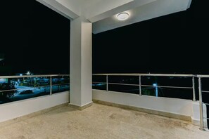 Ein Balkon mit Metallgeländer, einer weißen Säule und Blick auf einen Parkplatz bei Nacht.