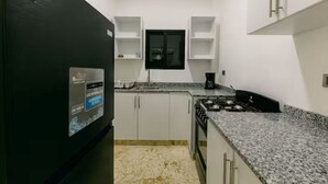 A kitchen with white cabinets, a black refrigerator, a gas stove, and a window above the sink. - Penthouse con dos camas grande A-301 (Punta Cana)