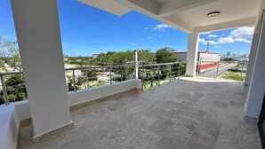 Un balcón abierto con vistas al entorno, incluyendo árboles y edificios.