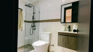 Une salle de bain moderne avec une douche à parois de verre, des toilettes blanches et un meuble-lavabo en bois avec un miroir.
